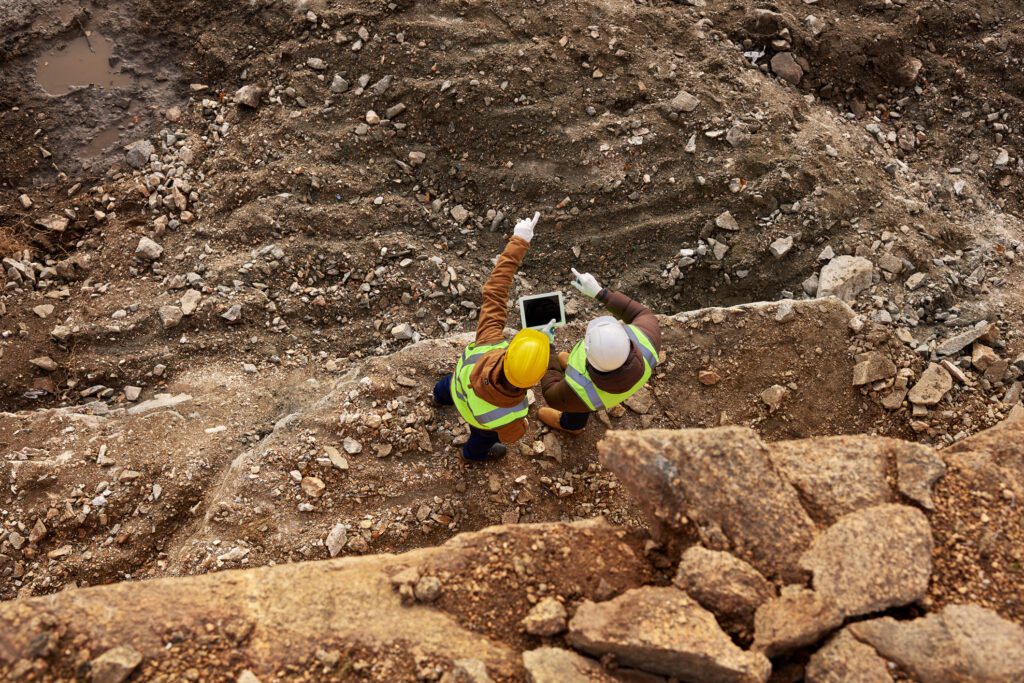 A man in yellow vest holding a tablet near rocks.